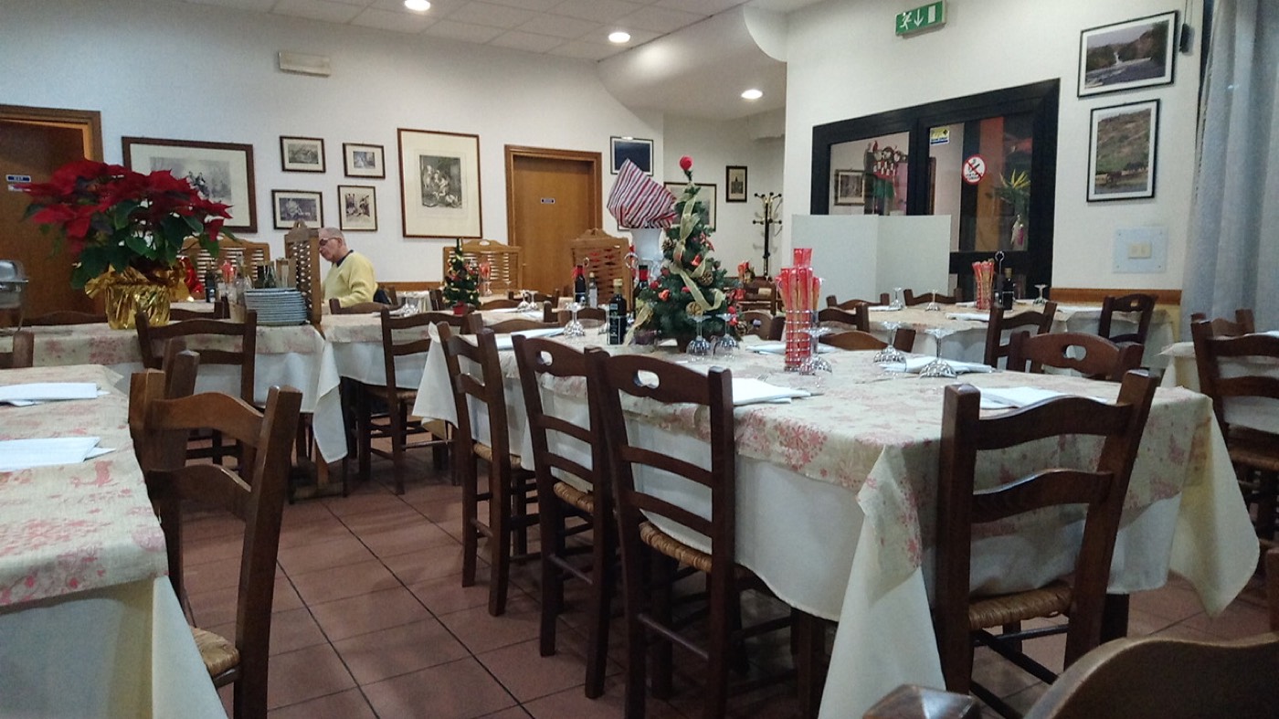 La sala della trattoria con tovaglie a fiori e sedie in legno